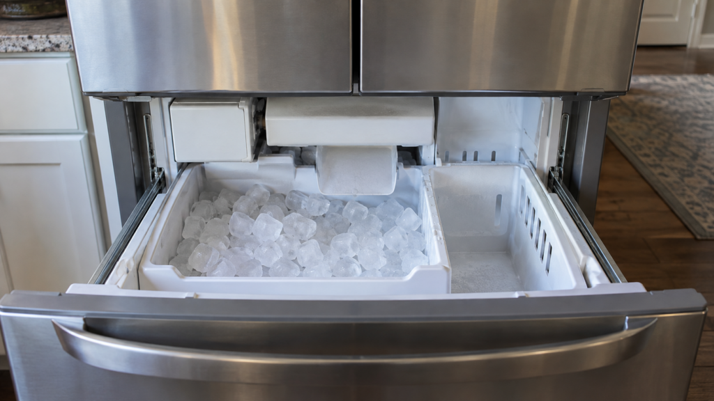 The open freezer drawer of an American refrigerator at eye level, the built-in ice bin and dispenser chute visible inside.